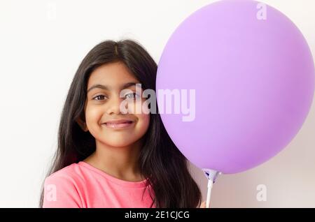 Porträt eines niedlichen und lächelnden kleinen indischen Mädchen hält einen lila Ballon in ihrer linken Hand Darstellung eines Geburtstags-Party-Konzept. Stockfoto