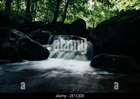 Wasserfall auf dem Fluss Jedlov im Isergebirge in der Nähe der polnischen Grenze. Im dunklen Wald gibt es einen kleinen Hoffnungsschimmer. Stockfoto