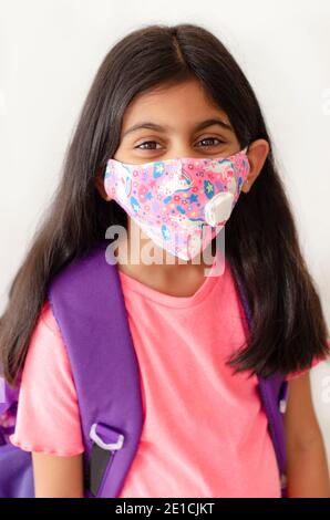 Lächelndes und glückliches kleines Indianerkind mit Gesichtsmaske und Schultasche, das nach covid-19 Quarantäne und Sperrung wieder in die Schule geht. BILDUNGSKONZEPT Stockfoto