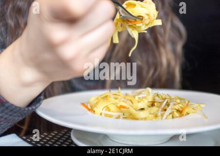 Nahaufnahme der Frau mit langen Haaren, Essen Tagliatelle Pasta mit Gemüsesauce Stockfoto