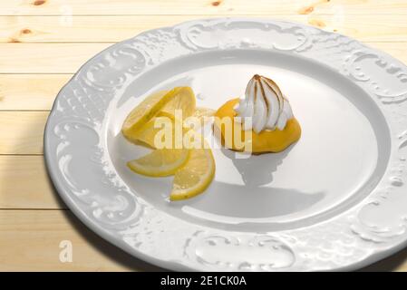 Zitronencreme-Tarte mit Baiser Brule und Zitronenscheiben Weißer Teller auf Holztisch Stockfoto