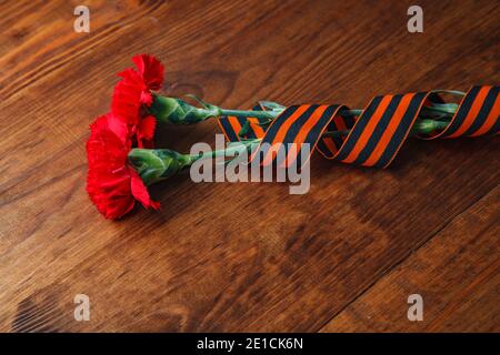 Zwei rote Blume und St. George's Band auf Holz- Hintergrund. selektive Fokus Bild Stockfoto