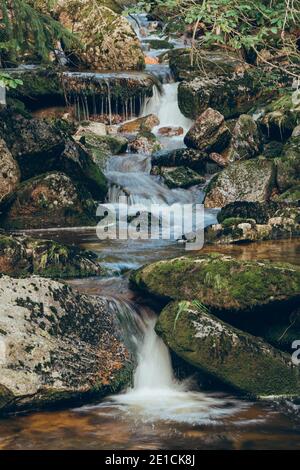 Kleiner Fluss im Isergebirge in der tschechischen Umgebung. Das Wasser findet einen Raum zwischen einem Kieshaufen und einem Wald. Stockfoto