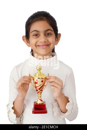 Portrait von einem schönen und lächelnden indischen Schulmädchen in weißem Hintergrund mit einer goldenen Trophäe und Darstellung Sieg. Stockfoto