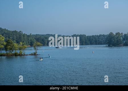 Ein paar Kajakfahrer und ein Motorboot, die einen Wake verursachen Vorbei mit den Wäldern im Hintergrund ein der see an einem heißen, nebeligen Tag im Sommer Stockfoto