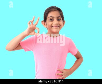 Portrait eines niedlichen kleinen indischen Mädchen in blauem Hintergrund zeigt "perfekte" Form Zeichen mit Händen und zum Ausdruck bringen Zufriedenheit und Wertschätzung. Stockfoto