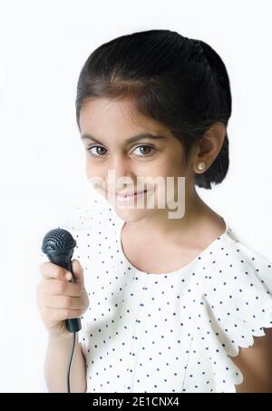 Schöne porträtit eines lächelnden indischen Kind in singenden Pose mit einem mike in weiß gekleidet halten.. Stockfoto