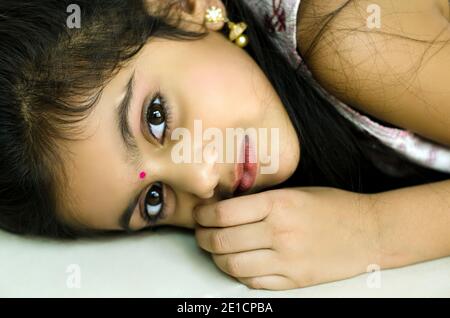 PORTRÄT EINES SCHÖNEN INDISCHEN MÄDCHEN IN ETHNISCHEN INDISCHEN TRAGEN MIT SCHMUCK UND MAKE-UP LIEGEND UND HALTUNG RELAXD GEKLEIDET. Stockfoto