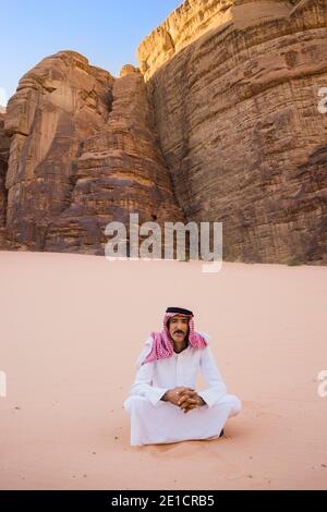 Ein arabischer Mann sitzt in der Wüste und trägt traditionelle arabische Kleidung Stockfoto