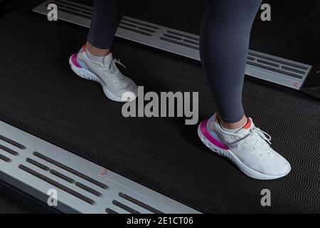 Fitness-Mädchen läuft auf dem Laufband. Frau mit muskulösen Beinen im Fitnessstudio Junge schöne Frau auf dem Laufband im Fitnessstudio. Nahaufnahmende Schuhe erscheinen. Stockfoto