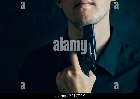 Guy mit Pistole bereitet sich auf Selbstmord zu begehen. Person in schwarzem Hemd Schnauze der Waffe zu Kinn. Depression mit tödlichem Ausgang. Stockfoto