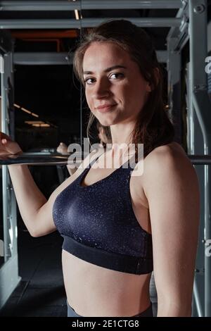 Schöne junge Fitness-Frau macht Kniebeugen mit einer Langhantel auf der Smith Machine im Fitnessstudio. Schöne Frau posiert für die Kamera. Stockfoto