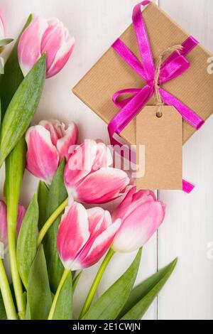 Happy Mothers Day Konzept. Draufsicht auf rosa Tulpen Bouquet und Geschenk mit leeren Karte auf weißem Holzhintergrund. Mutter und Kind emotionale Verbindung versteckt Stockfoto