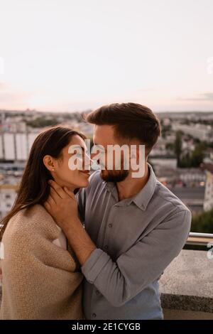 Nahaufnahme Porträt, Mann und Frau lächeln einander bei Sonnenuntergang mit Stadt im Hintergrund. Romantische Momente im intimen Kreis Stockfoto