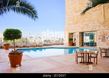 Blick auf den Pool auf der Dachterrasse des Grand Hyatt Amman, Jordanien. Tisch und Stühle zum Abendessen mit der König-Abdullah-I-Moschee und dem Stadtbild von Amman in der Ferne. Stockfoto