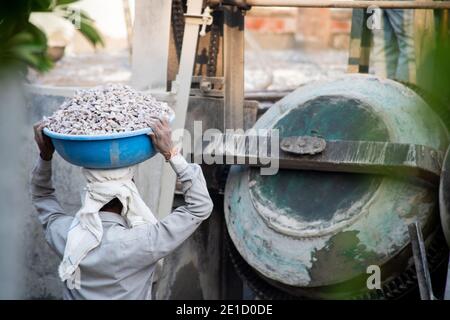 Zoomed in Schuss von indischen unterprivilegierten Bauarbeiter mit Sand, Zement, Steine und Wasser auf dem Kopf, um in einen Mixer zu laden, um zu machen Stockfoto