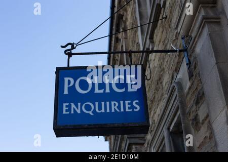 Ein altes, beleuchtetes blaues öffentliches Informationsschild "Police Enquiries", das vor der Polizeistation in Leyburn, North Yorkshire, England, hing Stockfoto