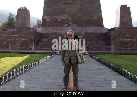 Peter Martin Rhind, der den Äquator in Ecuador vor dem Äquatordenkmal in Quito überspannt. Stockfoto