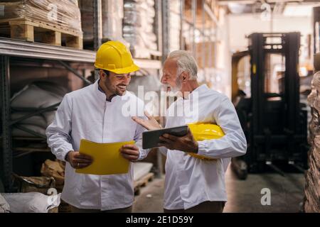 Teamarbeit. Bild von zwei Mann Lager Mitarbeiter lächeln und Blick zusammen auf digitale Tablet. Ältere Hochschule lernt jüngere ein, wie man ein löst Stockfoto