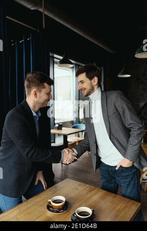 Lächelnde junge Geschäftspartner in Business Casual Wear blicken einander an und schütteln nach Vereinbarung die Hände. Grußkonzept Stockfoto