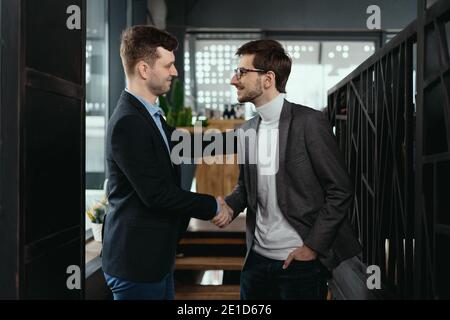 Lächelnde junge Geschäftspartner in Business Casual Wear blicken einander an und schütteln nach Vereinbarung die Hände. Grußkonzept Stockfoto