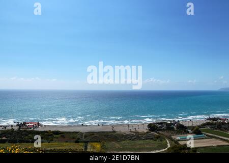 Blauer Himmel und blaues Meer mit durchschnittlichen Wellen an der Küste. Blick auf Kourion Strand bei sehr starker Sonne. Riesiger Strand in Südzypern, ideal für Surfer und Wasser spo Stockfoto