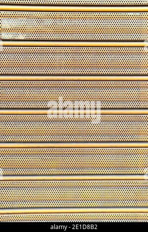 Geriffelte, perforierte Metallblechoberfläche mit Perforationen und Löchern. Abstrakter vertikaler gestreifter Hintergrund. Geschlossener Ladeneingang. Lockdown-Konzept Stockfoto