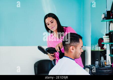 Professionelle Friseur latin Frau Schneiden Haare mit Haarschneidemaschine und Kamm zu einem Mexikaner, der in Mexiko Frisur bekommt Stadt Stockfoto