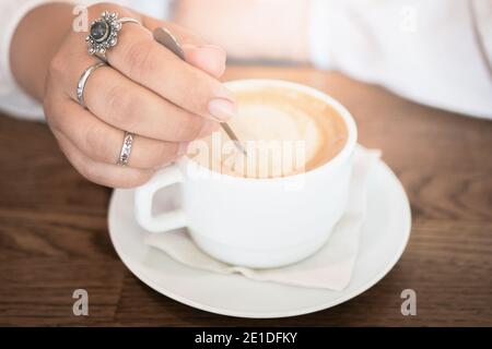 Kaffee spät in weißer Tasse und weibliche Hand mit Löffel, Nahaufnahme. Good Morning Konzept Idee. Stockfoto