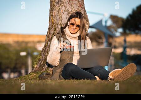 Frau sitzt im Freien mit Kreditkarte und mit Laptop. Online-Shopping Stockfoto