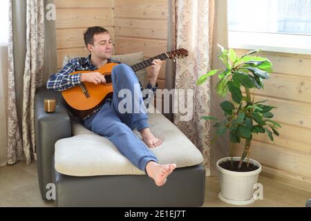 Junger Mann spielt Gitarre und sitzt am Wochenende auf dem Sofa Morgen Stockfoto