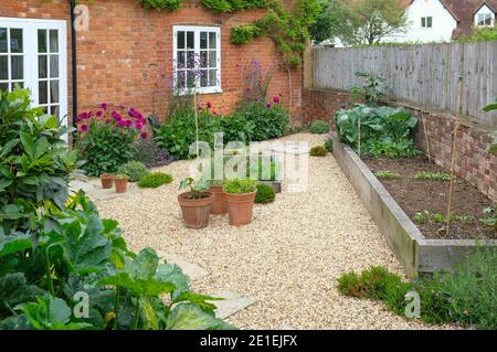 Garten eines viktorianischen englischen Hauses, Großbritannien. Schotter- und Eichenschläfer Hochbetten mit Blumen und Gemüse Stockfoto