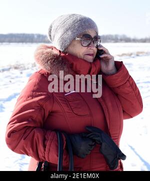 Russische ältere Frau im Telefongespräch gegen schneebedeckten Feld. Winter Stockfoto