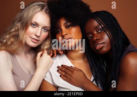 Junge hübsche kaukasische, afro, skandinavische Frau posiert fröhlich zusammen auf braunem Hintergrund, Lifestyle diverse Nationalität Menschen Konzept Stockfoto