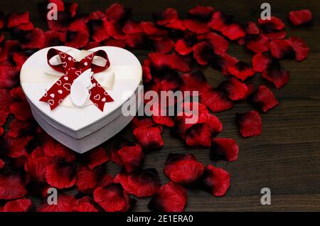 Herzförmige Geschenkbox auf roten Rosenblättern und Holz Tabelle als Kopierbereich Stockfoto