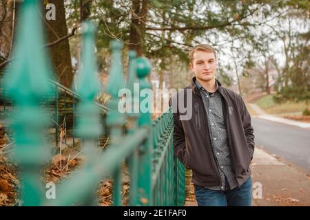 Ein ernsthafter junger Mann lehnt sich an einen schmiedeeisernen Zaun Im Herbst Stockfoto