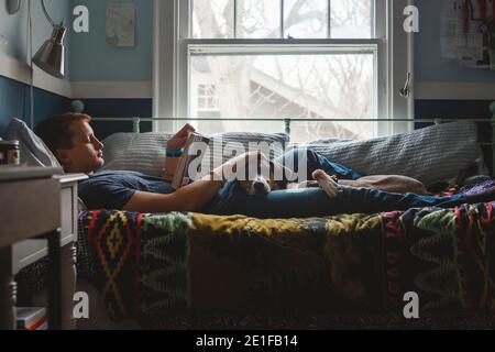 Ein junger Mann liegt auf dem Bett Streichelhund in seinem Runde und ein Buch lesen Stockfoto