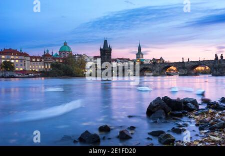 Schwäne schwimmen in der Moldau in der Nähe der Karlsbrücke gegen den Himmel bei Sonnenuntergang, Prag, Böhmen, Tschechische Republik Stockfoto