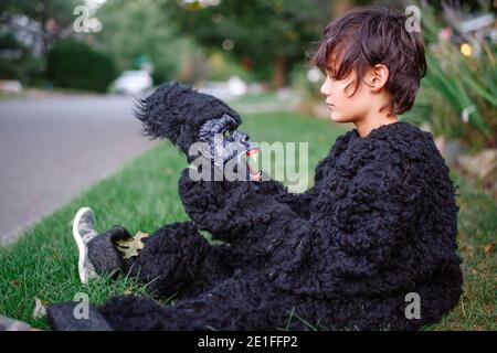 Ein Junge sitzt im Gras im Gorilla Anzug und schaut zu Gruselige Gorilla Maske Stockfoto