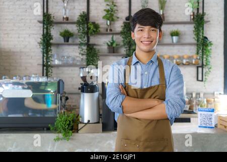 Asian Mann Barista oder Besitzer kleines Unternehmen in Schürze suchen An Kamera und Arm gekreuzt im modernen Café Stockfoto