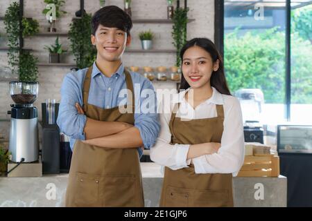 Asiatisches Paar Barista oder Inhaber kleines Unternehmen in Schürze suchen An der Kamera bereit, Kaffee-Service in der modernen geben Café-Bar Stockfoto
