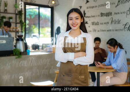 Asiatische Frau Barista oder Besitzer kleines Unternehmen in Schürze suchen An der Kamera bereit, Kaffee-Service mit dem Kunden in geben Hintergrund bei der modernen Kaffee s Stockfoto