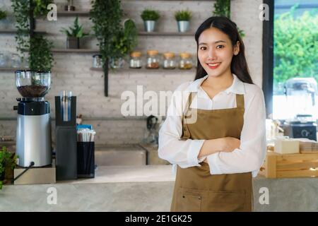 Asian Mann Barista oder Besitzer kleines Unternehmen in Schürze suchen An Kamera und Arm gekreuzt im modernen Café Stockfoto