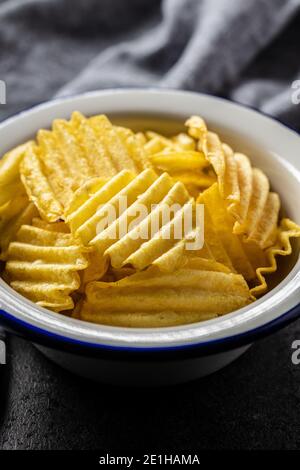 Knusprige Kartoffelchips in der Schüssel auf dem schwarzen Tisch. Stockfoto