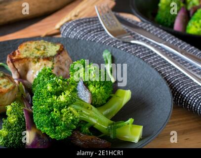 Gedämpfte Broccoli-Röschen auf einem dunklen Teller mit Fleisch Stockfoto