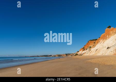 Ein Blick auf einen weiten leeren goldenen Sandstrand mit Bunte Sandklippen an einem sonnigen Tag Stockfoto