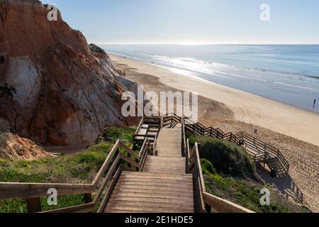 Eine lange Holzpromenade Zugang zum Strand führt hinunter zu einem Breiter goldener Strand mit bunten Sandklippen Stockfoto