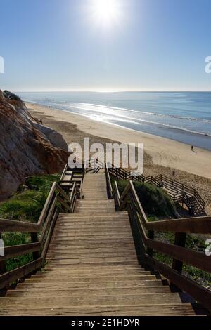 Eine lange Holzpromenade Zugang zum Strand führt hinunter zu einem Breiter goldener Strand mit bunten Sandklippen Stockfoto