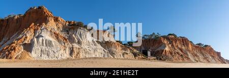 Ein Panoramablick auf einen weiten leeren goldenen Sandstrand Mit bunten Sandklippen an einem sonnigen Tag Stockfoto