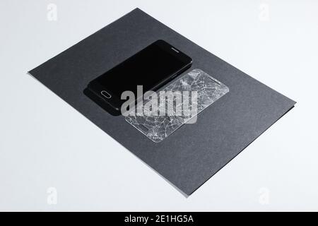 Smartphone mit gebrochenem Schutzglas auf Papierhintergrund. Seitenansicht Stockfoto